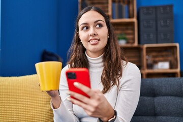 Young beautiful hispanic woman using smartphone drinking coffee at home