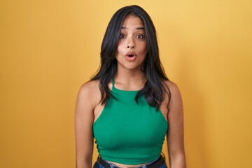 Brunette woman standing over yellow background afraid and shocked with surprise and amazed expression, fear and excited face.