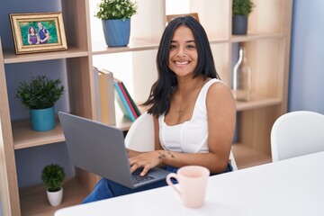 Fototapeta premium Young hispanic woman using laptop sitting on table at home
