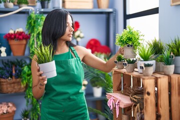 Young hispanic woman florist holding plants at florist shop
