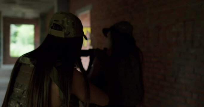 sexy girls are rescuing their friends, aiming and moving in with the rifle in abandoned building. back view slow motion