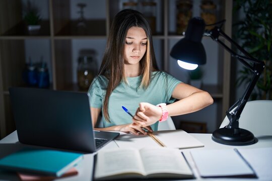 Teenager girl doing homework at home late at night checking the time on wrist watch, relaxed and confident