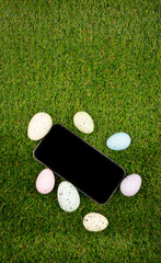 Phone with blank empty screen on background of easter eggs with  in  on green grass. Space for text. Happy Easter! Smartphone mockup, top view