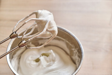 Mixer beaters with whipped egg whites. Whipped egg whites and other ingredients for cream or as an ingredient for baking on wooden table, closeup