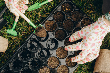 A woman prepares the ground for planting seeds in cells in the spring. Close-up hands are running with the earth.