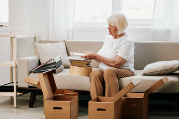 Fototapeta na wymiar elderly woman sits on a sofa at home with boxes. collecting things with memories albums with photos and photo frames moving to a new place cleaning things and a happy smile. Lifestyle retirement.