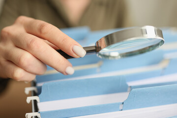 Hand of woman holding magnifier glass above folders