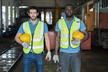 Two male engineer worker working in industry factory, standing holding industrial equipment tools, wearing safety uniform and helmet. Group of male technician worker at work in locomotive garage