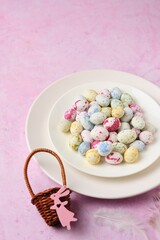 Sugar candy in the form of bird eggs on a white plate on a pink concrete background.