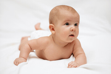 A newborn baby in a diaper is lying on stomach on a white background and looking to the side.
