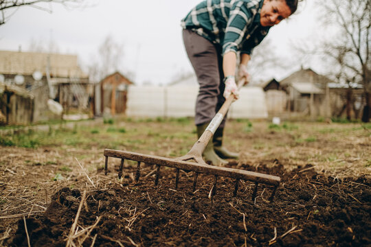 Young woman farmer works with a rake in a field in spring. Preparing the soil before planting. Close-up of a rake in the hands of a woman.