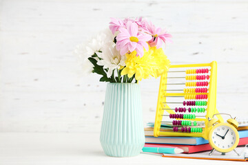 Bouquet of colorful chrysanthemums in vase, abacus, alarm clock and notepads on white wooden background with copy space. Concept teachers day