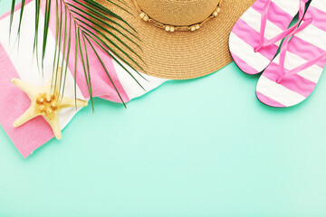Pair of flip flops with straw hat, towel, starfish and palm leaf on mint background