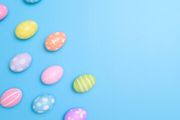 Happy Easter holiday greeting card design concept. Colorful Easter Eggs and spring flowers on blue background. Flat lay, top view, copy space.