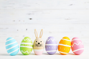 Egg with rabbit face and row colorful easter eggs on white wooden background
