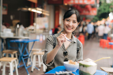 Happy young Asian woman backpack traveler enjoying street food at China town street food market in Bangkok, Thailand. Traveler checking out side streets.