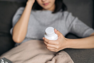 Asian woman with cold and flu reading instructions on medicine bottle