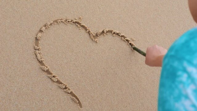 Wave washes away the heart drawn by the girl on the sand.