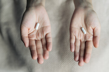 Female hands hold and offer two choice medicine pills capsule for chosen. White and pink candy or meds compare to choose from. Concept decision making or indecisiveness. - obrazy, fototapety, plakaty