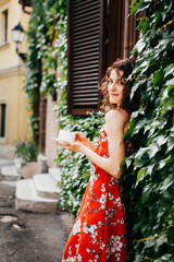 Young beautiful woman in a red dress with a cup on  European street