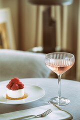 Elegant set table with raspberry dessert and a glass of champagne. Trendy interior background.