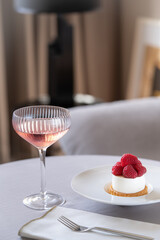 Elegant set table with raspberry dessert and a glass of champagne. Trendy interior background.