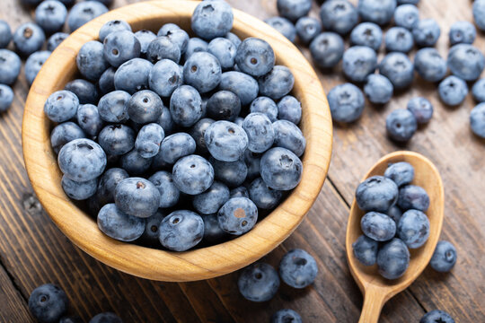 Ripe blueberries in a wooden bowl and spoon on a background of scattered berries. Concept of healthy and dieting eating.