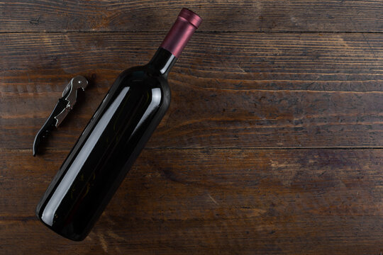 Corkscrew and a bottle of red wine on a wooden background. Top view