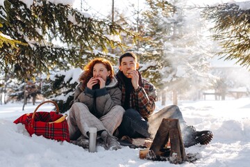 A young married couple had a picnic in a snowy forest. A beautiful red-haired woman sits together...