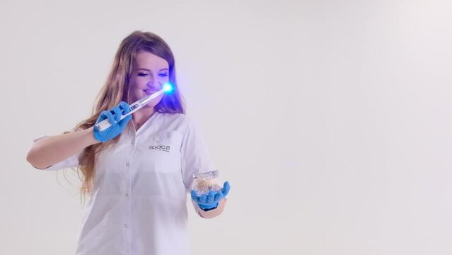 Photopolymer lamp Doctor Fairy with a glowing blue lamp in a white medical suit Dentist treatment of teeth prosthetics put fillings treat gums caries beautiful woman on white background studio ad