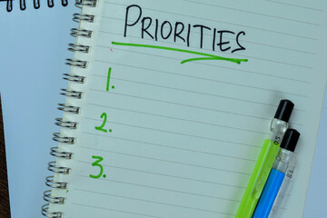 Concept of Priorities write on book. Supported by an additional services isolated on Wooden Table.