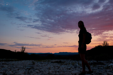 A silhouette of a female traveler standing in the mountains during sunset