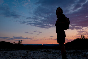 A silhouette of a female traveler standing in the mountains during sunset