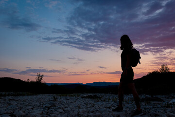 A silhouette of a female traveler standing in the mountains during sunset