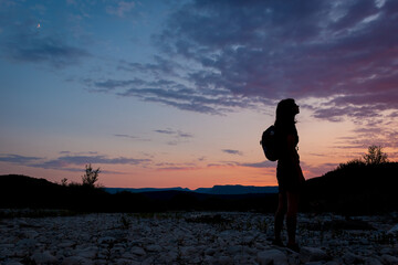 Fototapeta premium A silhouette of a female traveler standing in the mountains during sunset