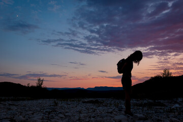 A silhouette of a female traveler standing in the mountains during sunset