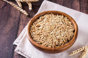 A plate with unpeeled oat seeds and ears of oats on a wooden table.