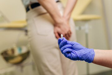 Woman at a proctologist's appointment. The doctor holds a rectal suppository before entering the...