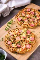 Appetizing pizza waffle with vegetables, sausages and cheese on a board on the table. Vertical view