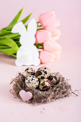 Happy easter nest with quail eggs and heart, white rabbit and tulips bouquet vertical view