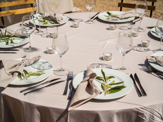 Wedding banquet concept. Chairs and round table for guests, served with cutler and, flowers and crockery and covered with a tablecloth