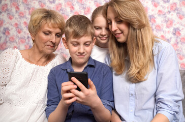 Fototapeta premium Happy grandchildren, grandmother and mother have fun using smartphone.