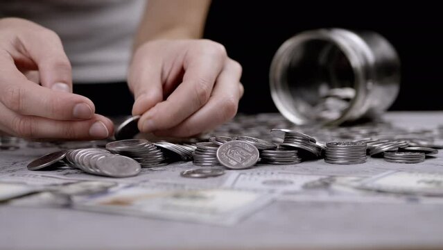 Female Hands Counting Coins that Spilled Out of Glass Piggy Bank on Table. Time-lapse. Scattering of Ukrainian silver five-cent. Budget, spending, savings, accumulation. Wealth, poverty. Stock. Penny.