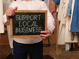 Support local business is shown using the text on a board held by a businessman - obrazy, fototapety, plakaty