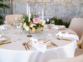 Wedding banquet concept. Chairs and round table for guests, served with cutler and, flowers and crockery and covered with a tablecloth