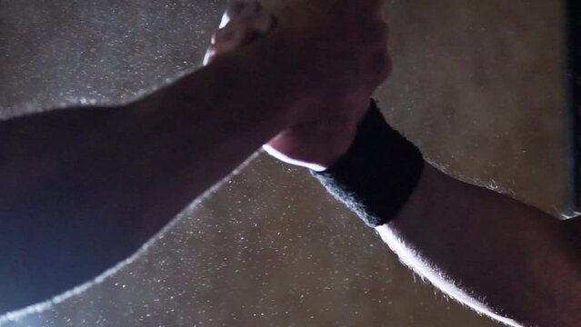 Strong with athletic body men greet and high-five each other close-up against the backdrop of light with smoke and magnesia in a dark gym, hands