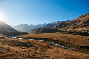a winding river flows in a valley between high autumn mountains on a sunny clear day with a clear blue sky