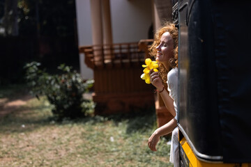 The wind blows through the brightly red hair of an attractive beautiful girl. A Caucasian girl on a tourist trip enjoys the ride in an authentic Indian rickshaw.