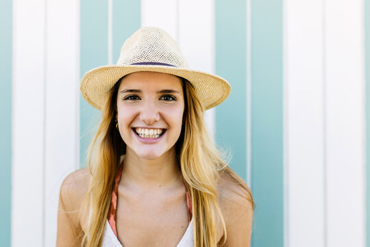 Smiling portrait of happy young trendy caucasian woman wearing summer hat standing outdoors