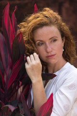 This portrait depicts a stunningly beautiful young woman with fiery red hair and a scattering of freckles across her cheeks and nose. The image evokes a carefree, summery feeling with its warm, golden